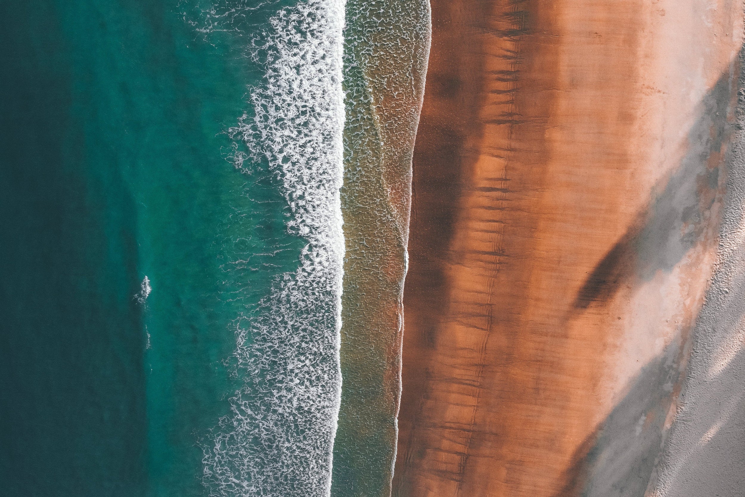 Aerial view of a coastal landscape with red cliffs and turquoise ocean water.
