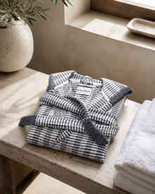Cote Jacquard Bathrobe in Salt & Stone — folded lifestyle shot on bathroom bench with towels